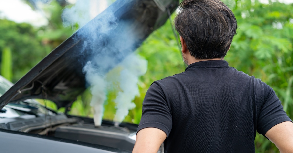 4 Common 6.0L Powerstroke Engine Problems A man wearing a black T-shirt stands back looking at the steam rising from the engine of a vehicle.